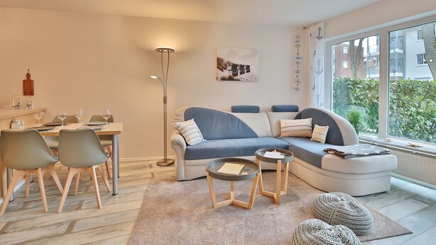 Ein modernes Wohnzimmer mit Sofa, Esstisch, Stühlen und einem großen Fenster.