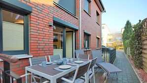 Un patio exterior con una mesa lista para comer, un edificio de ladrillo y un sendero que lleva a una zona vallada.