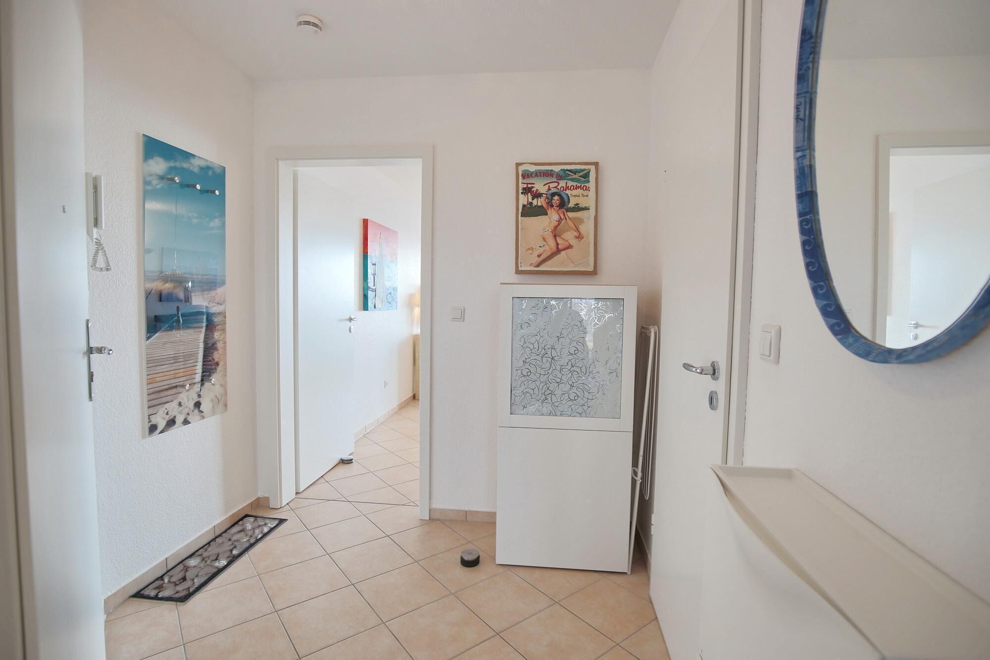 A hallway with a refrigerator, a door with a mirror, and a poster on the wall.