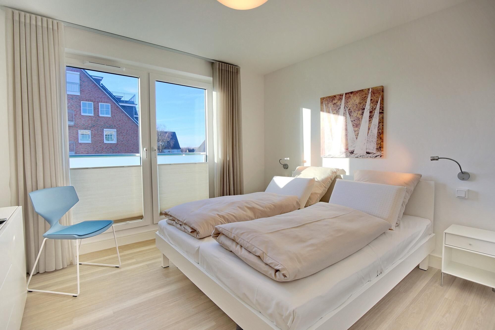 A modern hotel room with a large bed, a chair, a desk, and a window with a view of buildings.