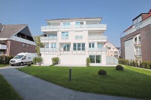 Un immeuble résidentiel moderne à plusieurs étages, doté de balcons, d’une allée pavée et d’une pelouse bien entretenue.