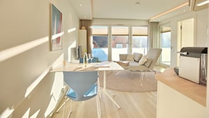 A modern living room with a sofa, a dining table, and a kitchen area. - Villa Seeperle II Herzmuschel Appartement 18 (Scharbeutz)