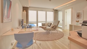 A modern hotel room with a dining area, a sofa, a desk, and a large window offering a view. - Villa Seeperle II Herzmuschel Appartement 18 (Scharbeutz)
