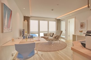 A modern hotel room with a dining area, a sofa, a desk, and a large window offering a view. - Villa Seeperle II Herzmuschel Appartement 18 (Scharbeutz)