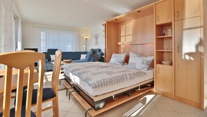 A compact bedroom with a bed, wooden wardrobe, and a small seating area with a sofa and chairs.