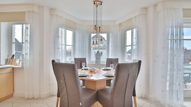 A dining area with a large table, four chairs, and a hanging light fixture.
