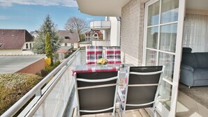 A balcony with a glass table and chairs, a small table with a flower, and a view of neighboring houses.
