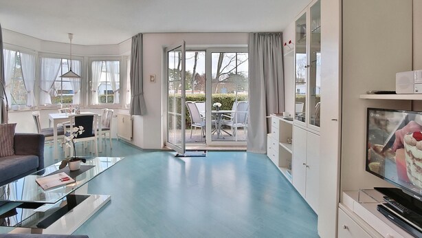 A modern hotel room with a glass coffee table, a sofa, a TV, and a view of the garden through the door. - Seesternresidenz Appartement 16 (Scharbeutz)