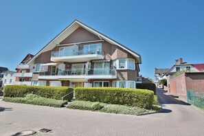 A two-story residential building with a balcony, a garage, and a paved driveway.