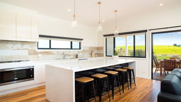 Una cocina moderna con una isla central, taburetes de bar y vistas a un campo verde.