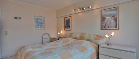 A bedroom with a bed, bedside tables, and wall-mounted lights.
