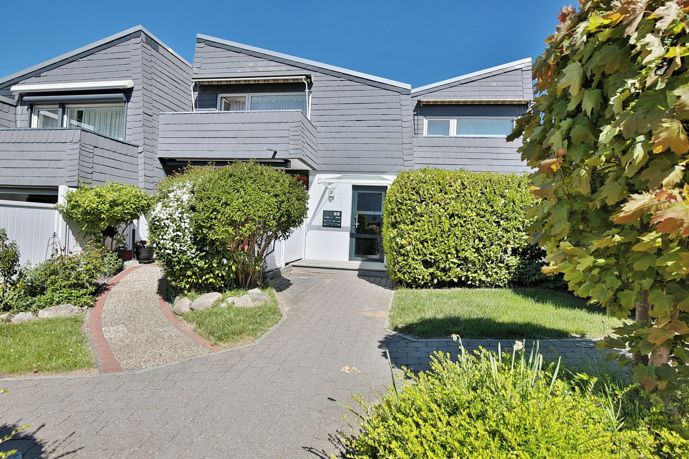 A modern two-story residential building with a paved driveway and well-maintained landscaping.