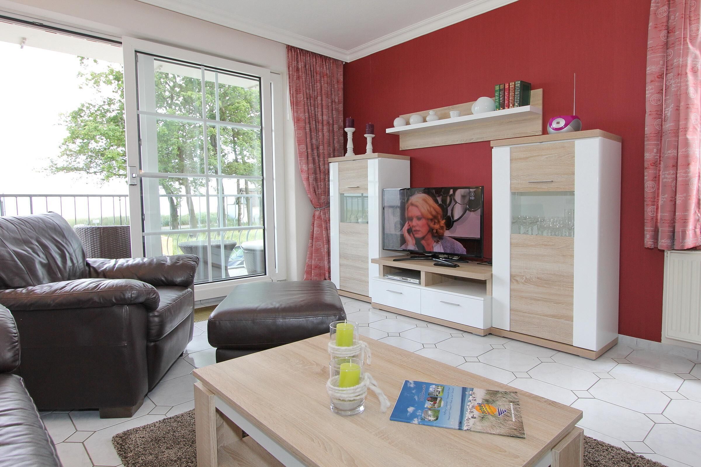 A living room with a brown leather sofa, a wooden coffee table with a magazine, and a TV on a white cabinet.