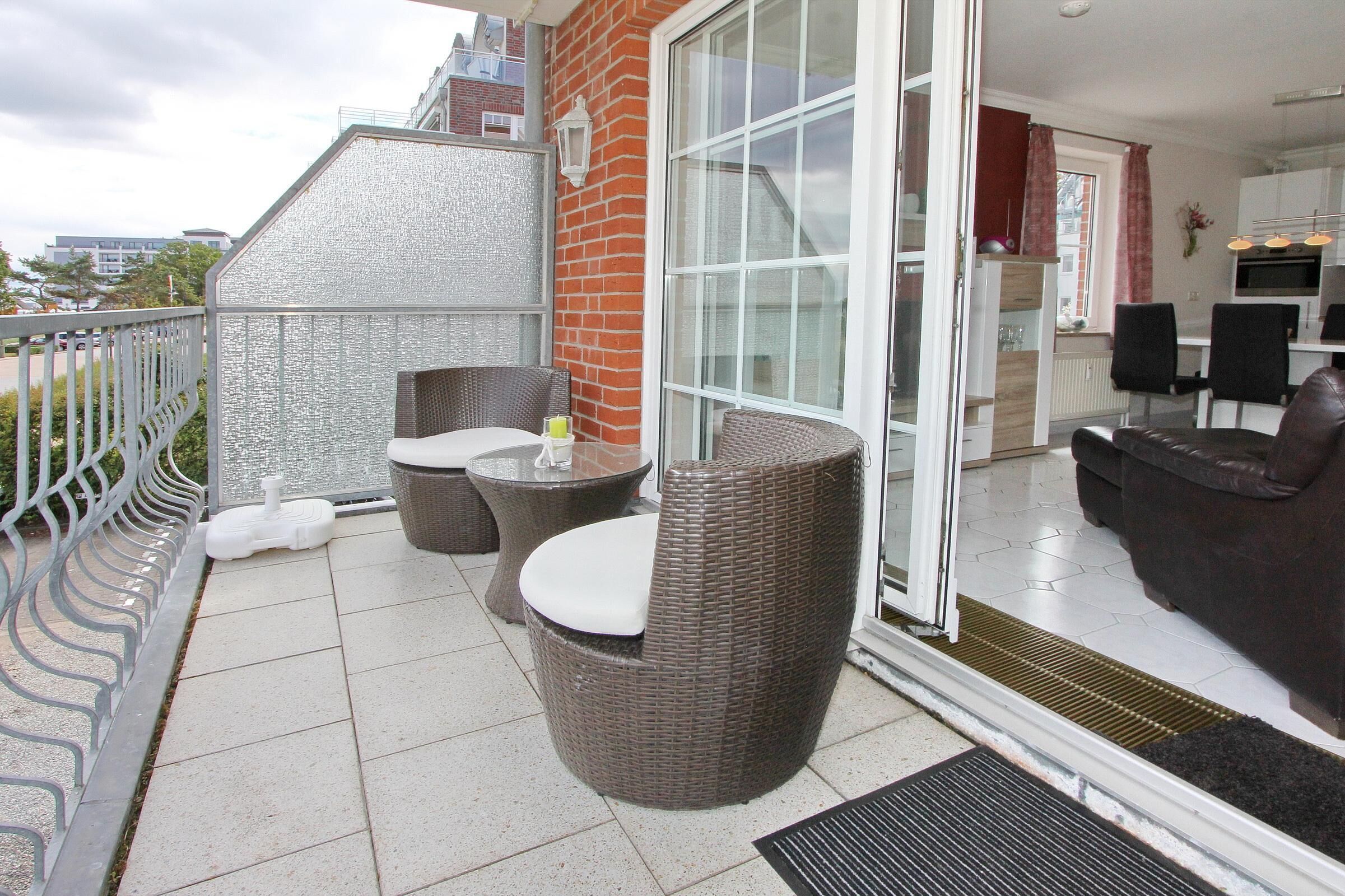 A balcony with wicker furniture, a glass door leading to a kitchen, and a view of the city.