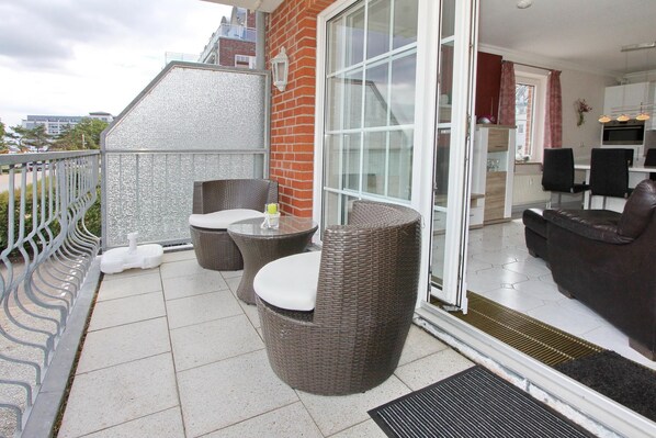 A balcony with wicker furniture, a glass door leading to a kitchen, and a view of the city. - Windrose Appartement 9 (Scharbeutz)