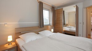 Ein Hotelzimmer mit einem großen Bett, Nachttischlampen, einem fenster mit Vorhängen und einem Spiegel.