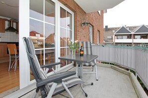 A patio with a table and chairs, a bottle of wine, and a vase with flowers.