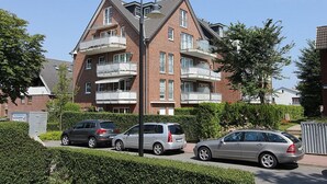 Ein mehrstöckiges Wohngebäude mit Balkonen, parkenden Autos und blauem Himmel.