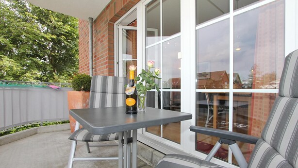 Eine Terrasse mit Tisch und Stühlen, einer Champagnerflasche und einem Blumenstrauß in einer Vase.