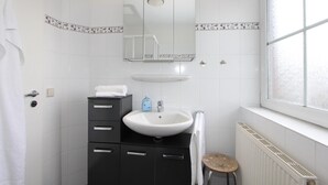 Ein Badezimmer mit einem weißen Waschbecken, schwarzen Schränken, einem Spiegel, einem Handtuchhalter und einem Fenster.