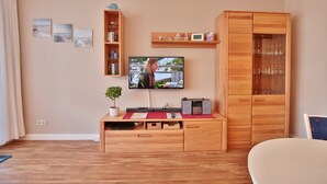 A living room with a wooden entertainment unit, a flat-screen TV, a bookshelf, and a cabinet with glass doors. - Strandburg Appartement 11 (Scharbeutz)