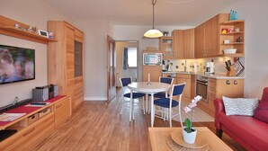A modern living room with a red sofa, a TV, wooden cabinets, and a dining area with chairs and a table. - Strandburg Appartement 11 (Scharbeutz)