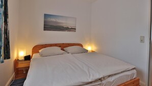 A neatly made bed with white linens, a wooden headboard, and a bedside table with a lamp. - Strandburg Appartement 11 (Scharbeutz)