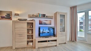 A modern living room with a wooden entertainment unit, a flat-screen TV, and a large window with curtains. - Barke Appartement 202 (Scharbeutz)
