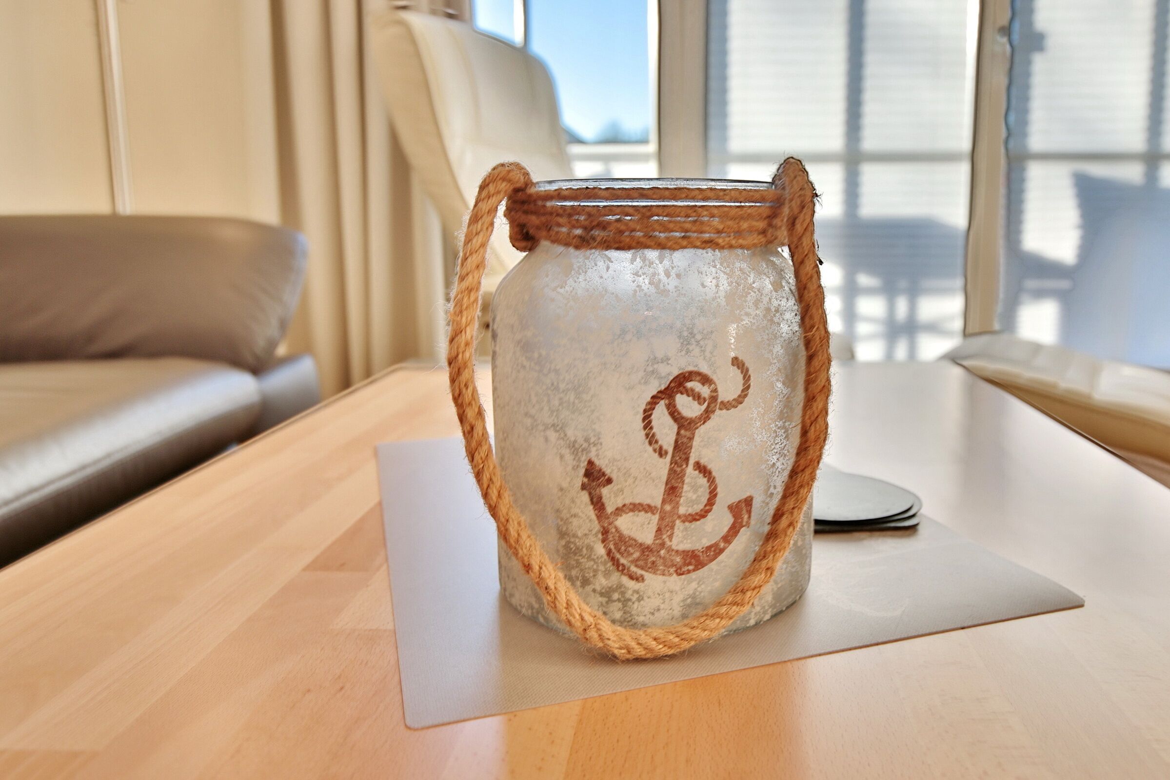 Ein rustikales Glas mit Anker-Design auf einem Holztisch in einem Raum mit Blick ins Freie.