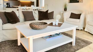 Ein modernes Wohnzimmer mit einem weißen Sofa, einem Couchtisch und einer Küche im Hintergrund.