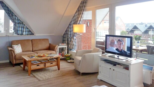 Een gezellige woonkamer met een bank, een bijzettafeltje, een televisie en een wit kastje.
