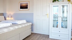 Een slaapkamer met een bed, een nachtkastje met lamp, een inloopkast met glazen deuren en een lijst met foto aan de muur.