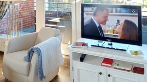 Een woonkamer met een televisie, een bank, een salontafel en een raam met uitzicht op huizen.
