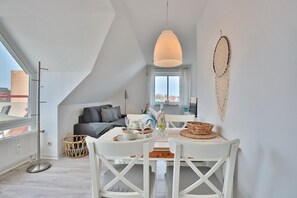 Ein modernes Loft-Apartment mit Essbereich, ausgestattet mit einem weißen Tisch und Stühlen, einer Pendelleuchte und Blick auf die Stadt durch große Fenster.