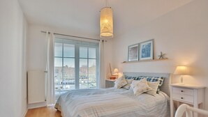 Une chambre à coucher comprenant un lit, des tables de chevet, un luminaire suspendu et une fenêtre avec des stores.