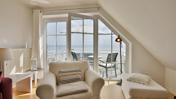 Un salon moderne doté d’une grande porte vitrée donnant sur un balcon avec vue sur la mer.
