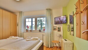 Une chambre d’hôtel avec deux lits, une fenêtre avec des rideaux, un radiateur, une petite table, une chaise, un téléviseur et un porte-manteau.