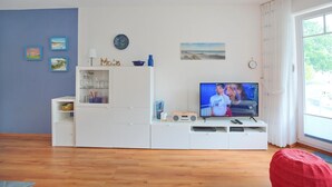 Un salon avec un téléviseur, un meuble de rangement blanc et des œuvres d’art accrochées au mur.