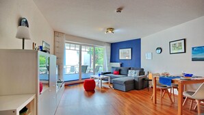 Un grand espace de vie comprenant un canapé, une table basse et une table à manger. On y trouve également un fauteuil en forme de poire rouge, un meuble blanc et un luminaire suspendu au plafond.