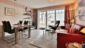 Ett modernt vardagsrum med ett glasbord, svarta stolar, en röd soffa och ett stort fönster med gardiner.