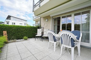 A patio with two white chairs and a table, a brick wall, and a window.
