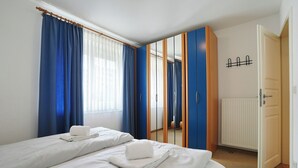 Habitación de hotel con dos camas, un armario, un radiador y una puerta con picaporte negro.