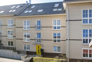 Un edificio residencial de varios pisos con fachada de ladrillo, varias ventanas y una puerta amarilla.