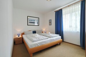Hotelkamer met een tweepersoonsbed, twee nachtkastjes, een raam met blauwe gordijnen en een aan de muur bevestigd schilderij.