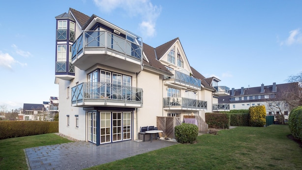 Une maison moderne à deux étages, dotée de grandes fenêtres, d’un patio couvert et d’une pelouse bien entretenue.