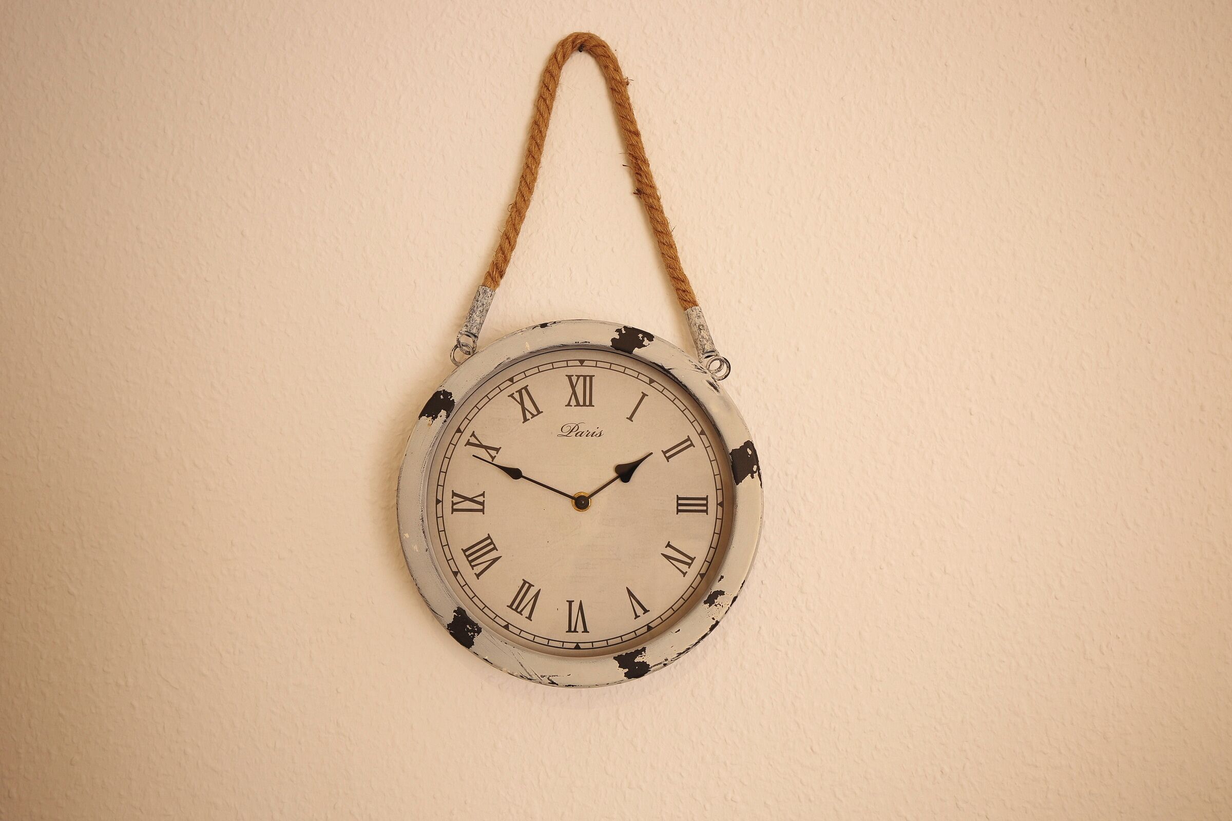 A wall-mounted clock with a rustic design, featuring Roman numerals and a rope handle.
