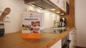 Uma cozinha com bancada de madeira, cafeteira e uma caixa identificada com "FRÜHSTÜCK TO GO", com imagens de alimentos.