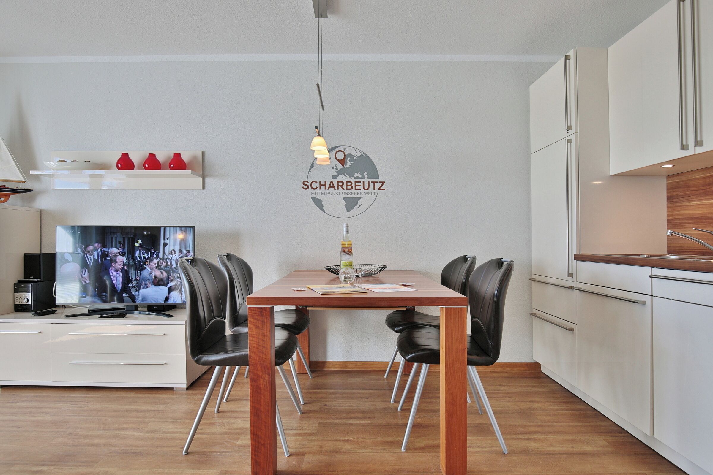 Uma sala de estar moderna com uma mesa de jantar, cadeiras pretas, uma TV e uma área de cozinha com armários.