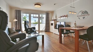 A modern living room with a sofa, chairs, a dining table, and a kitchen area. - Strandvilla Appartement 3 (Scharbeutz)