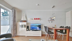 A modern living room with a television, a sailboat model, and a dining area with chairs and a table. - Strandvilla Appartement 3 (Scharbeutz)
